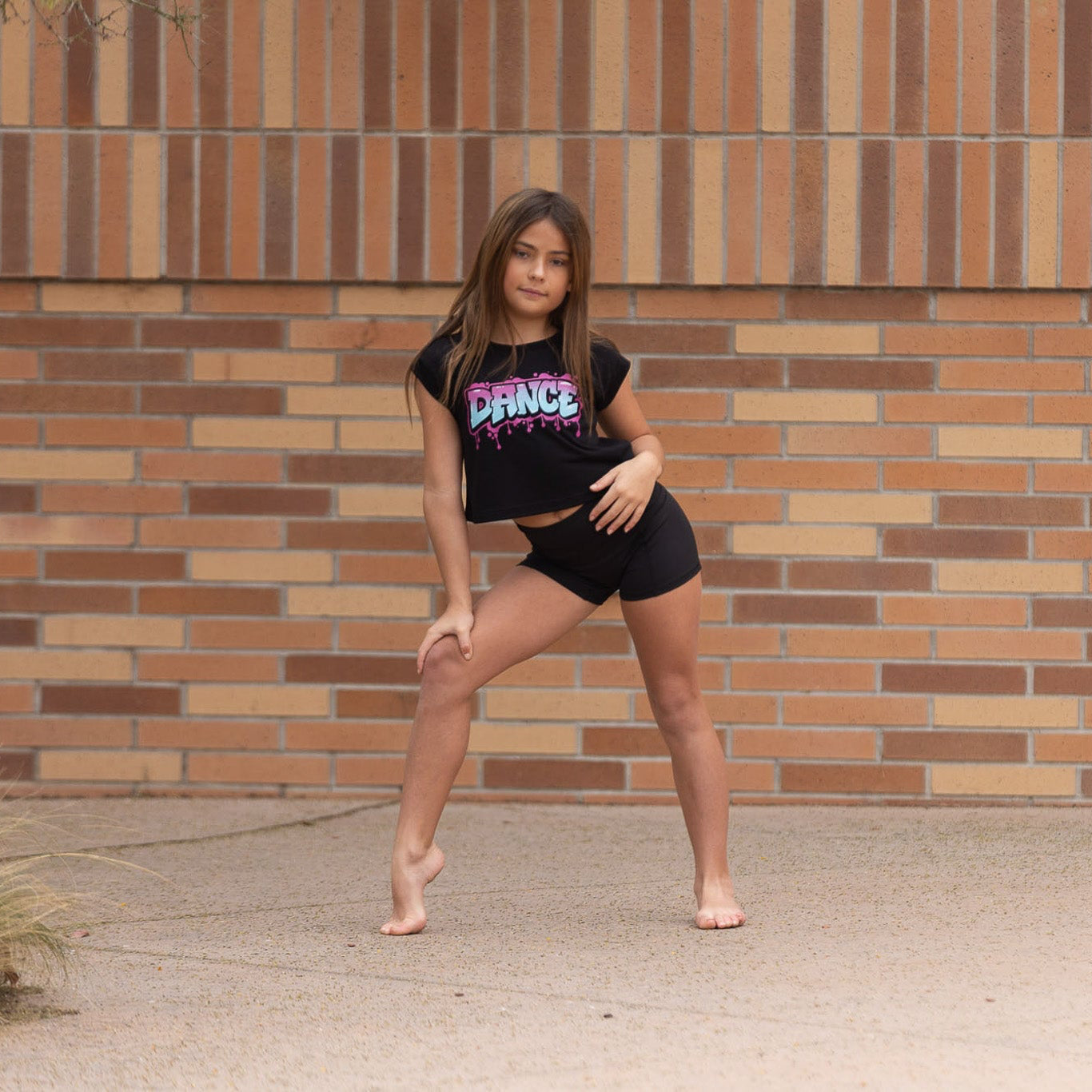 Young girl posing in front of a brick wall wearing a black 'DANCE' t-shirt.